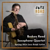 A man seated and holding a saxophone while looking into the camera