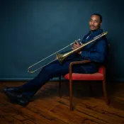 Man holding a trombone while sitting in a chair.