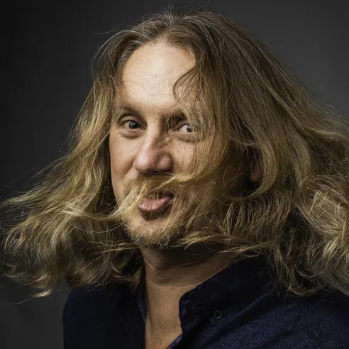 Man with shoulder-length dirty blond hair, whipping his head around.