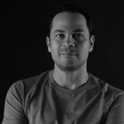 Person with short hair wearing a t-shirt, smiling with arms crossed.