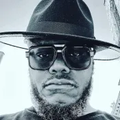 Man wiht a mustache and beard wearing a hat and large glasses.