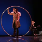 Person in a costume on a stage holding a large hoop with a keyboardist in the background.