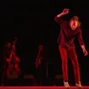A man on stage who looks to be dancing while musicians play in the background. 
