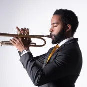 Man wearing a grey suit and yellow tie playing a trumpet with his eyes closed.