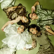 Four people wearing earth tones and flowy clothes lying on a green floor.