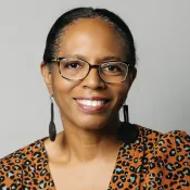 Person wearing long earrings, glasses, and smiling.
