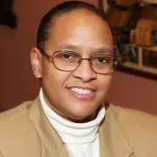 Person wearing glasses, a white turtle neck, and tan jacket.