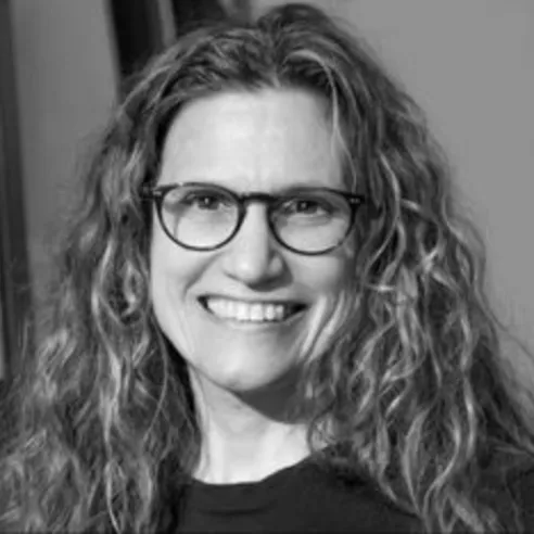 Woman with wavy hair and glasses smiling.