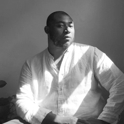 Man in a gauzy white button-up shirt with streams of light shining on him.